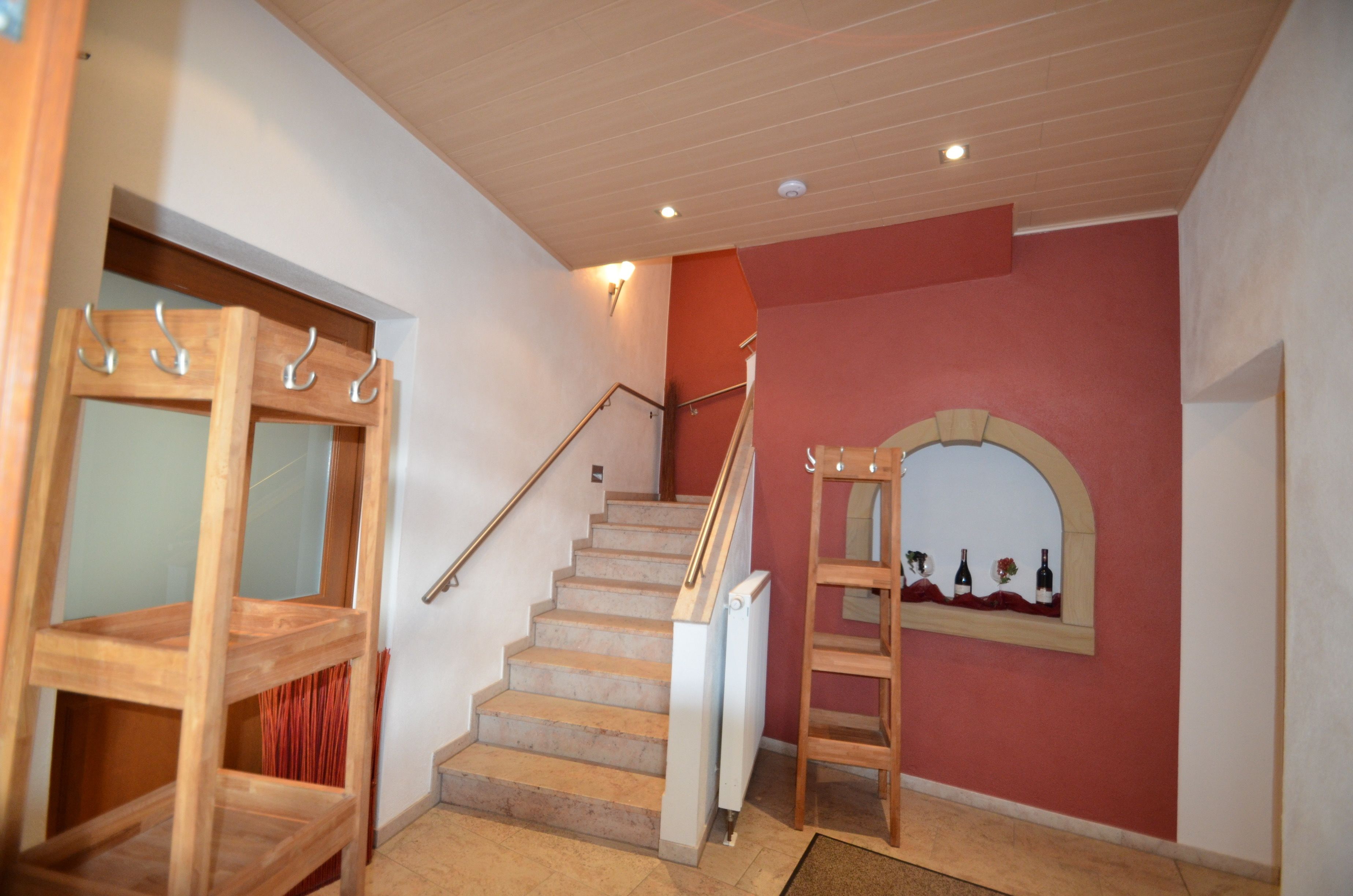 Una escalera con barandillas de madera, un pasamanos y un estante en la pared con botellas de vino.