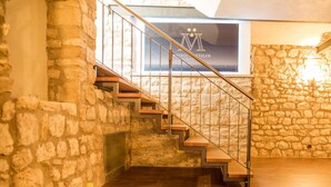A stone-walled room with a wooden staircase and a wine display. - Hofgut Metzler (Gau-Heppenheim)