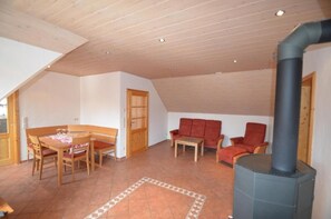 A cozy living room with a wooden ceiling, a dining table with chairs, a sofa, and a fireplace. - Hofgut Metzler (Gau-Heppenheim)