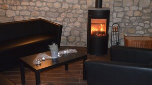 A stone wall, a black sofa, a wooden coffee table with decorative items, and a wood-burning stove. - Hofgut Metzler (Gau-Heppenheim)