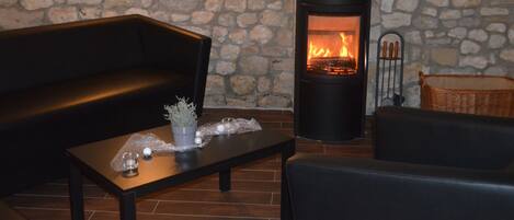 A stone wall, a black sofa, a wooden coffee table with decorative items, and a wood-burning stove.