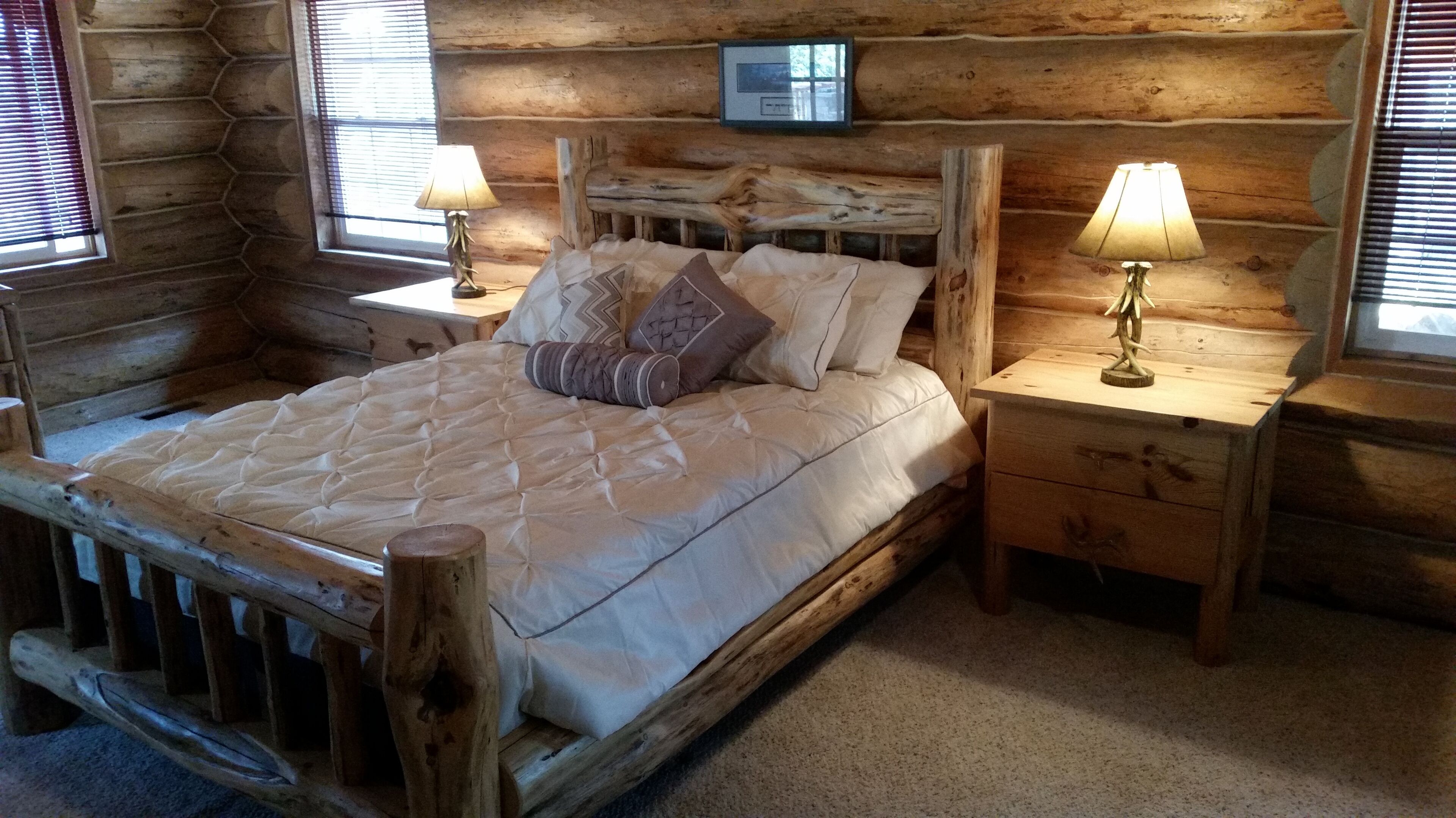 Une chambre à coucher dans un chalet en rondins, avec un grand lit, deux tables de chevet avec des lampes et un tableau accroché au mur.