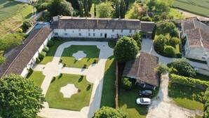 Vista aérea de una extensa propiedad con un jardín de diseño simétrico, varias construcciones y automóviles estacionados.