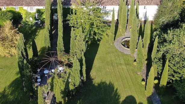 Vista aérea de una propiedad con un patio central, rodeado de altos cipreses y un edificio con techo de tejas.