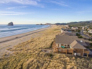 Una casa costera con playa de arena y vista al océano, que cuenta con una terraza amplia y varias habitaciones.