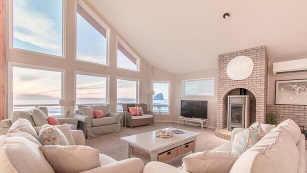 A spacious living room with large windows, a fireplace, and a television. - Top O' the Dune · Luxury Oceanfront, Huge home & views, game room (Pacific City)