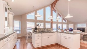A spacious kitchen with white cabinets, granite countertops, and large windows offering views of the ocean. - Top O' the Dune · Luxury Oceanfront, Huge home & views, game room (Pacific City)