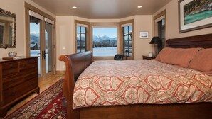 A bedroom with a large bed, a dresser, a mirror, and a view of mountains through the door.