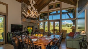 A spacious dining area with a large wooden table, multiple chairs, a fireplace, and a view of mountains through large windows.