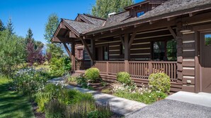 A log cabin with a porch, surrounded by a garden with various plants and flowers.