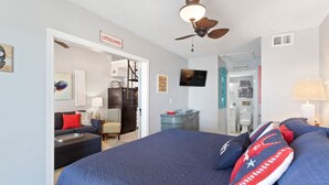 A bedroom with a bed, a ceiling fan, a TV, and a door labeled "Lifeguard". - Farm-Chic, Updated, 2 BR Condo, Pool, Lagoon Access, Walk To Beach! Cove 208A (Gulf Shores)