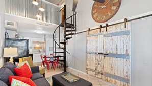 A modern living room with a spiral staircase, a large rustic clock, and a sliding barn-style door. - Farm-Chic, Updated, 2 BR Condo, Pool, Lagoon Access, Walk To Beach! Cove 208A (Gulf Shores)