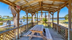 A wooden gazebo with a picnic table, surrounded by a wooden deck and lattice railings, overlooking a lake with houses in the background. - Farm-Chic, Updated, 2 BR Condo, Pool, Lagoon Access, Walk To Beach! Cove 208A (Gulf Shores)
