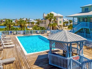 A wooden deck with a pool, lounge chairs, and a gazebo.