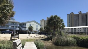 A wooden pier leading to a beach area with a building in the background. - Farm-Chic, Updated, 2 BR Condo, Pool, Lagoon Access, Walk To Beach! Cove 208A (Gulf Shores)
