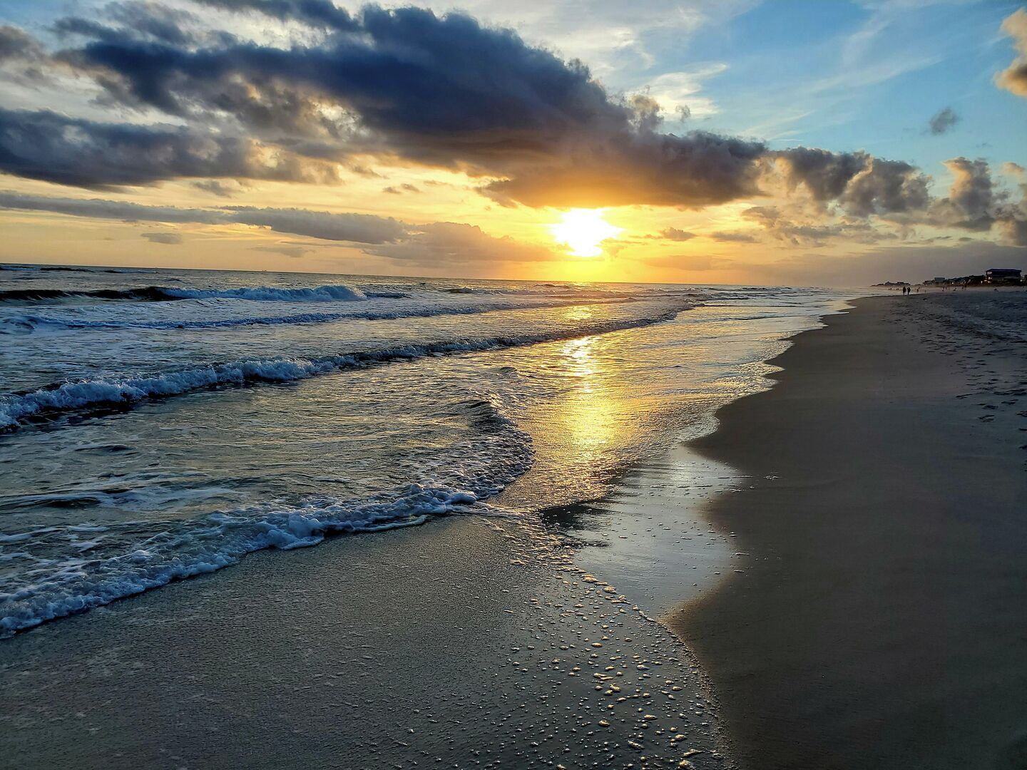 A beach with waves, a sunset, and a distant shoreline with buildings.