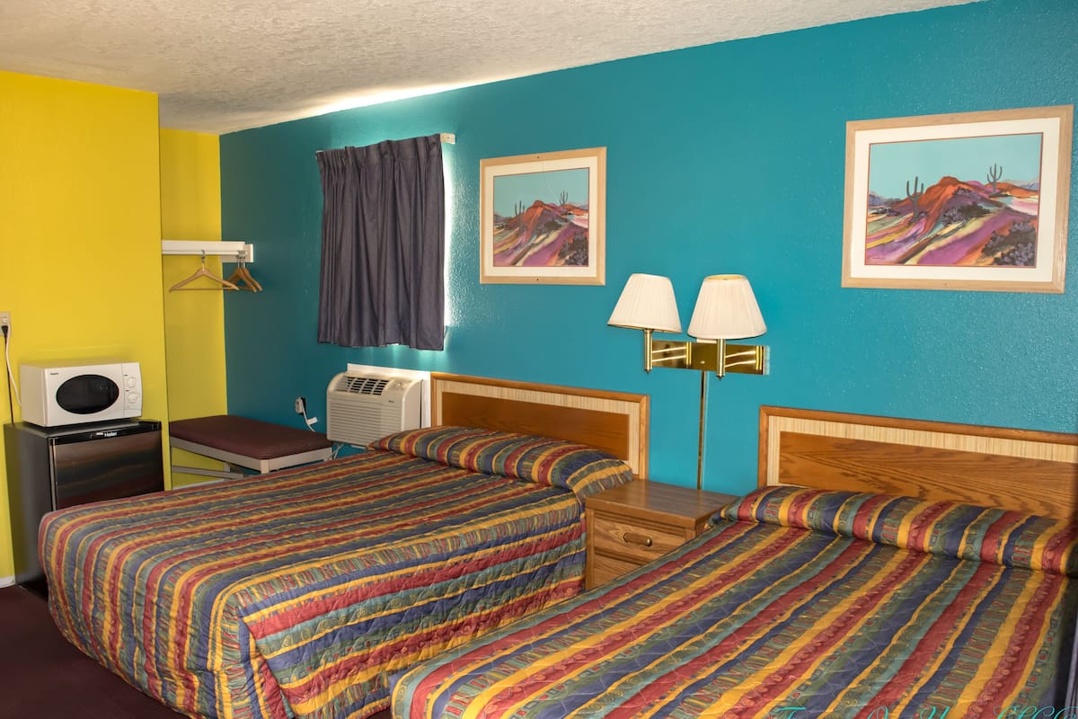 A room with two beds, a desk, an air conditioning unit, and a wall-mounted lamp.