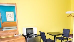 Habitación compacta con cama, un escritorio pequeño, refrigerador, microondas, dos sillas y cómoda de madera.