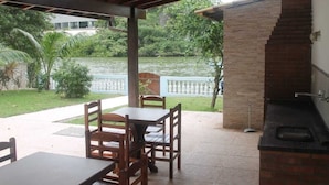 Un patio exterior con una parrilla de ladrillo, mesa y sillas de madera, y vista a un lago.