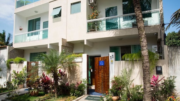 Un edificio moderno de varios pisos con un balcón, una puerta de madera y un jardín bien cuidado con diversas plantas.