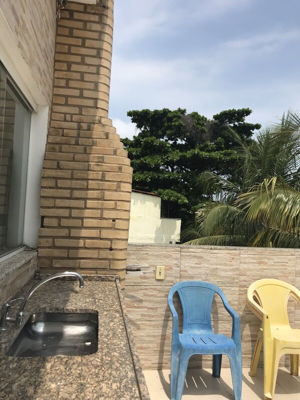 A kitchen area with a sink, a brick wall, and two plastic chairs. - Pousada Barra da Tijuca (Rio de Janeiro)