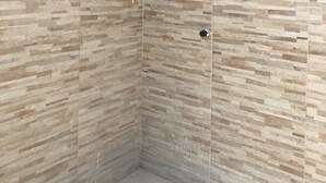 Ducha en esquina con cabezal de ducha tipo lluvia, una ventana y un interruptor de luz en la pared.