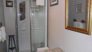 A bathroom with a glass-enclosed shower, a sink, a mirror with a decorative frame, and a small stool.