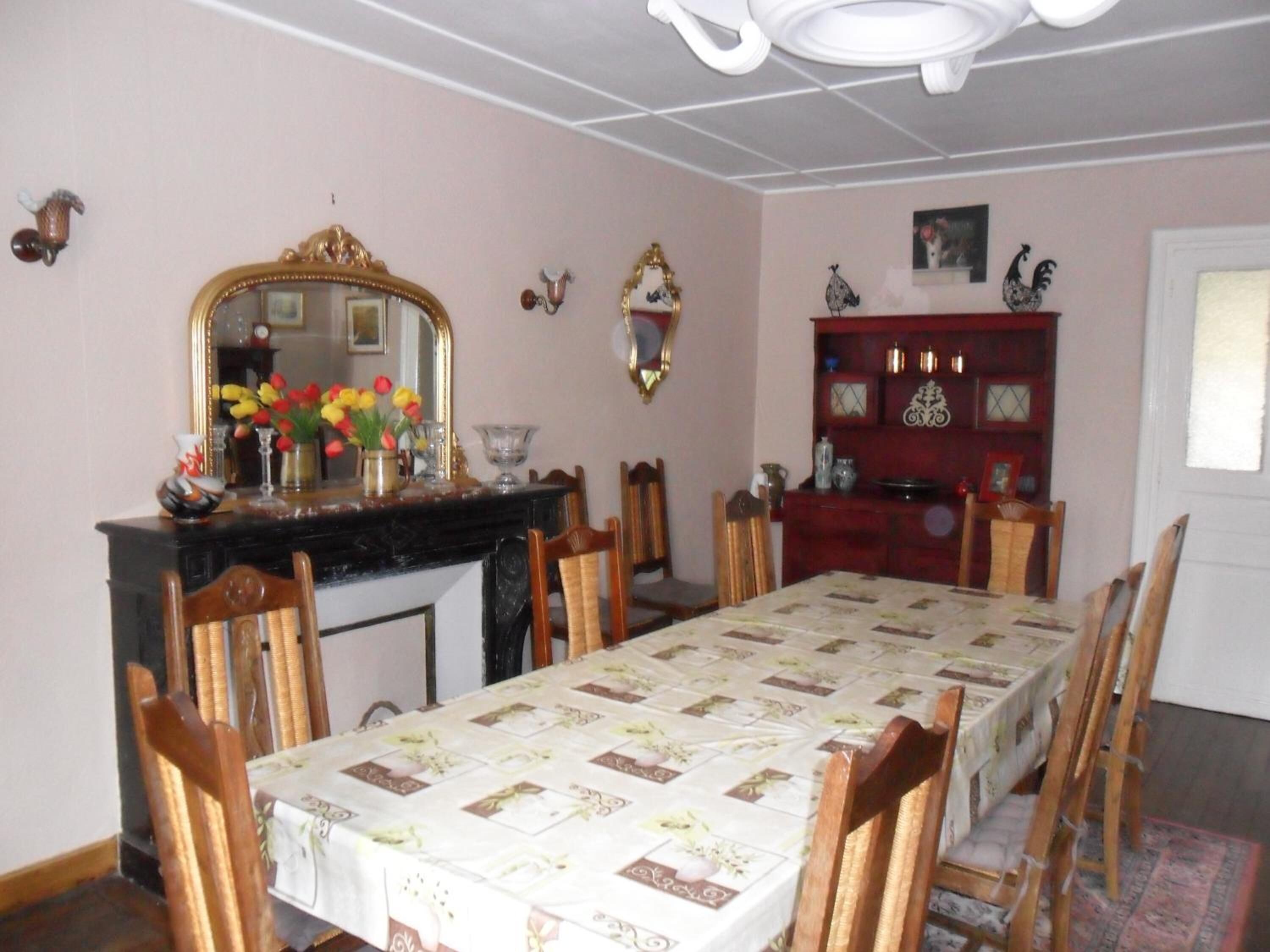 Een eetkamer met een lange tafel, stoelen, een open haard, een spiegel en een rode kast met decoratieve objecten.