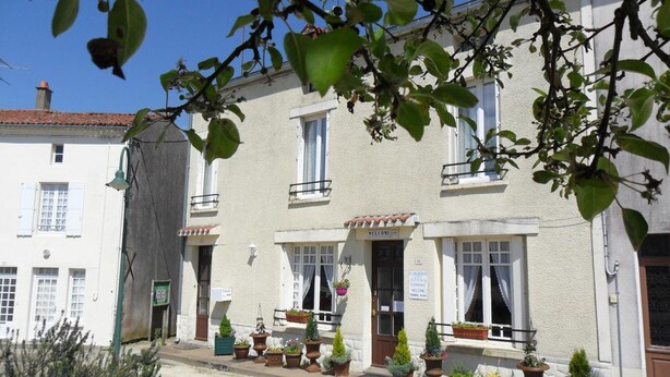 Un bâtiment à deux étages, doté d’une enseigne accueillante, de nombreuses fenêtres et de plantes en pot au rez-de-chaussée.