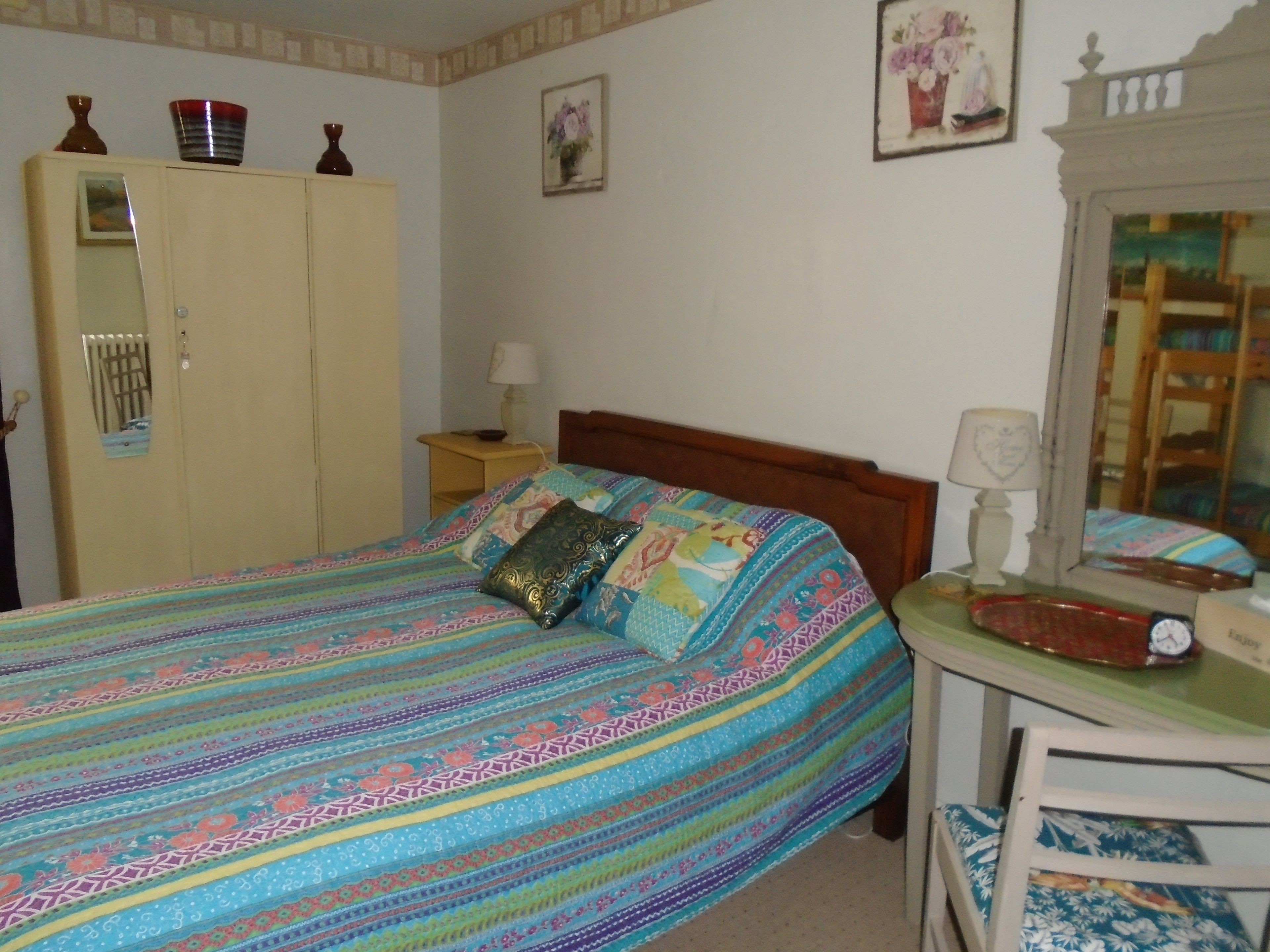 Ein Schlafzimmer mit einem Bett, einem Kleiderschrank, einem Nachttisch, einem Spiegel und einem Sessel.