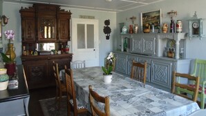 Un coin repas avec une table dressée pour quatre personnes, entourée de chaises en bois. Un luminaire blanc est suspendu au plafond au-dessus de la table.
