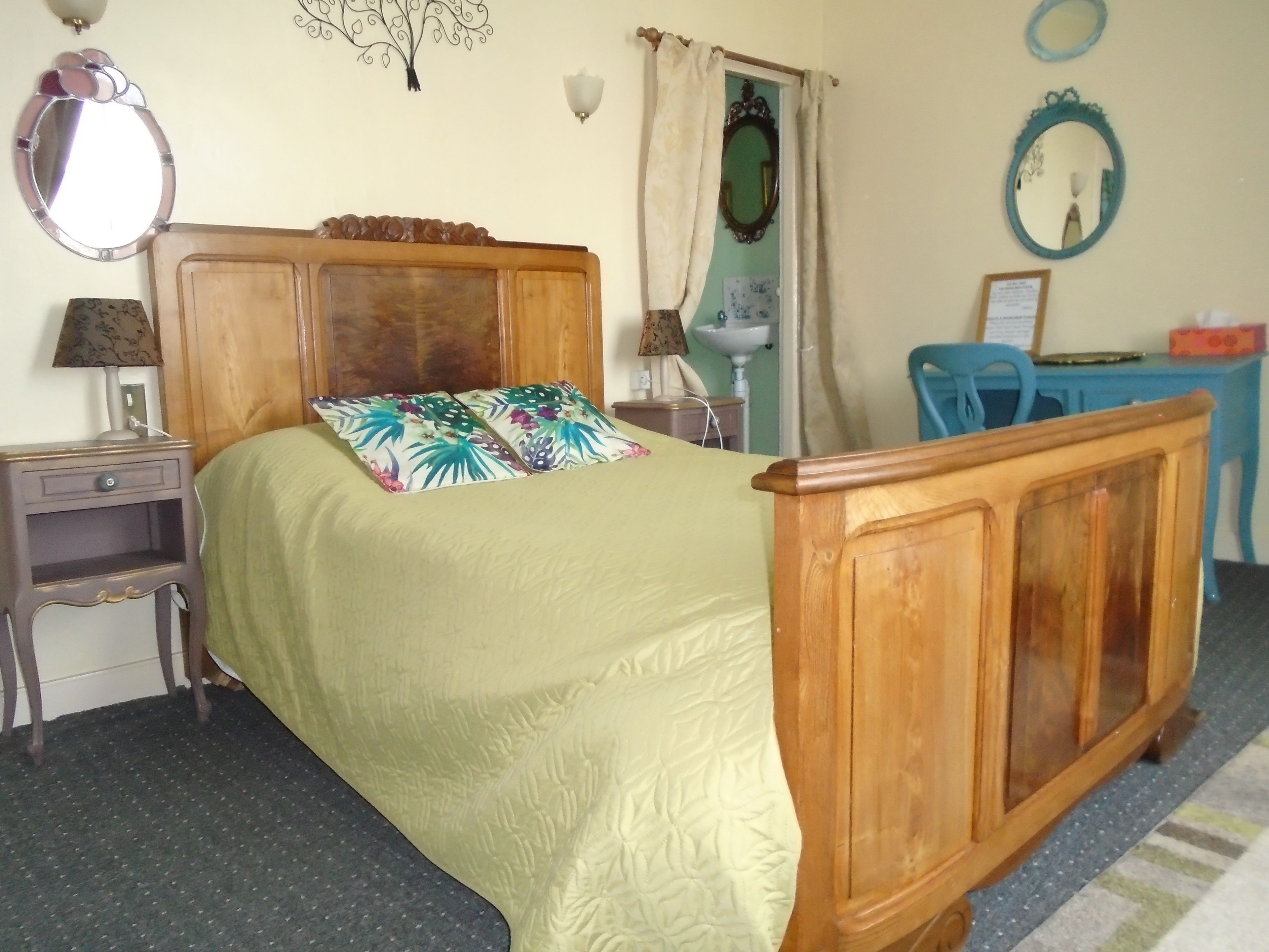 A bedroom with a wooden bed, a nightstand, a desk, a chair, and a mirror.