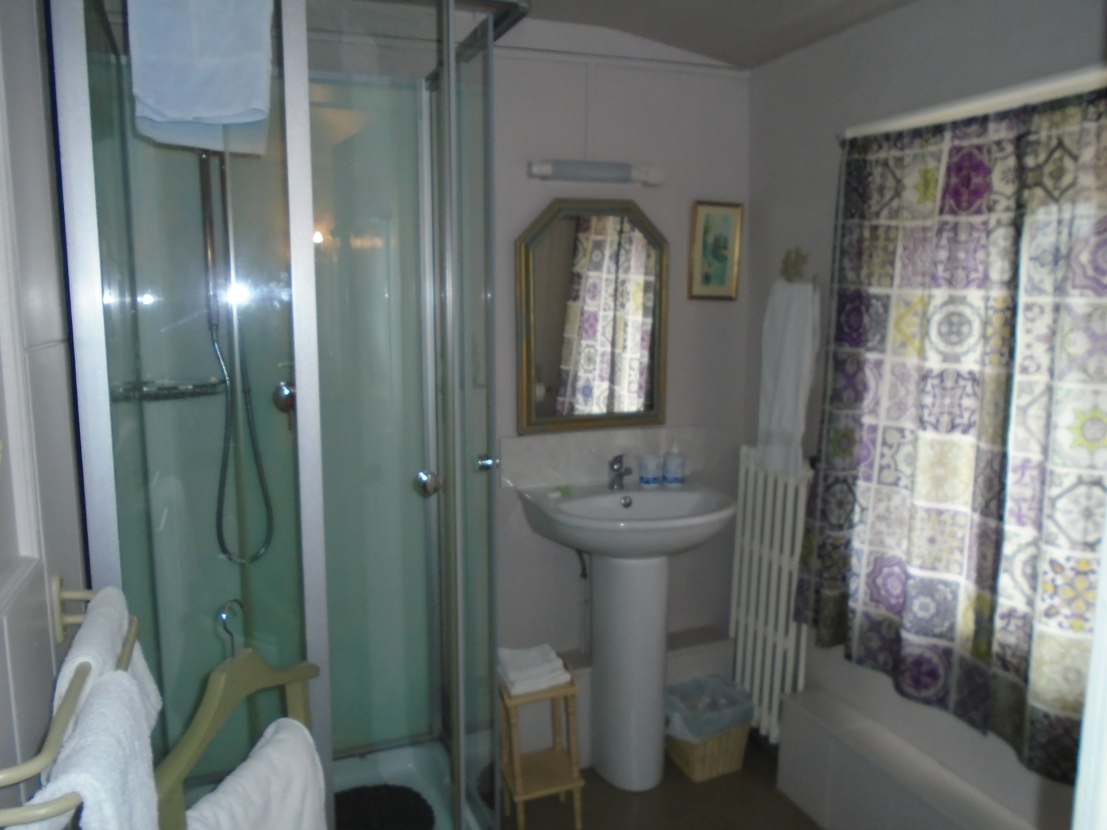 A bathroom with a glass shower enclosure, a sink, a small stool, and a radiator.