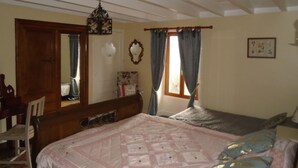 Une chambre à coucher avec un lit, une chaise, une commode, un miroir et une fenêtre avec des rideaux.