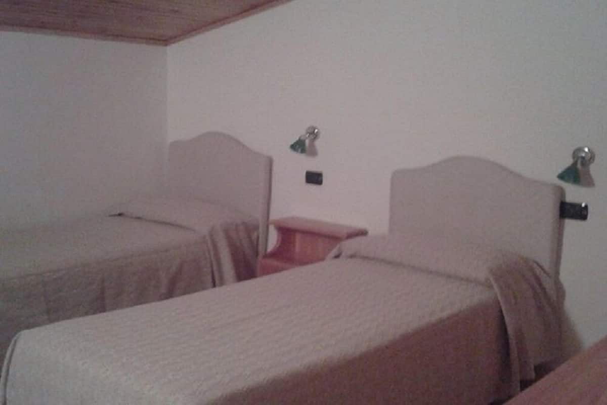 A room with two beds, a small table, and a wall-mounted lamp.