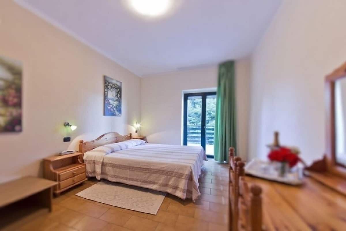 A bedroom with a bed, bedside tables, a nightstand, a window with curtains, and a small table with a vase.