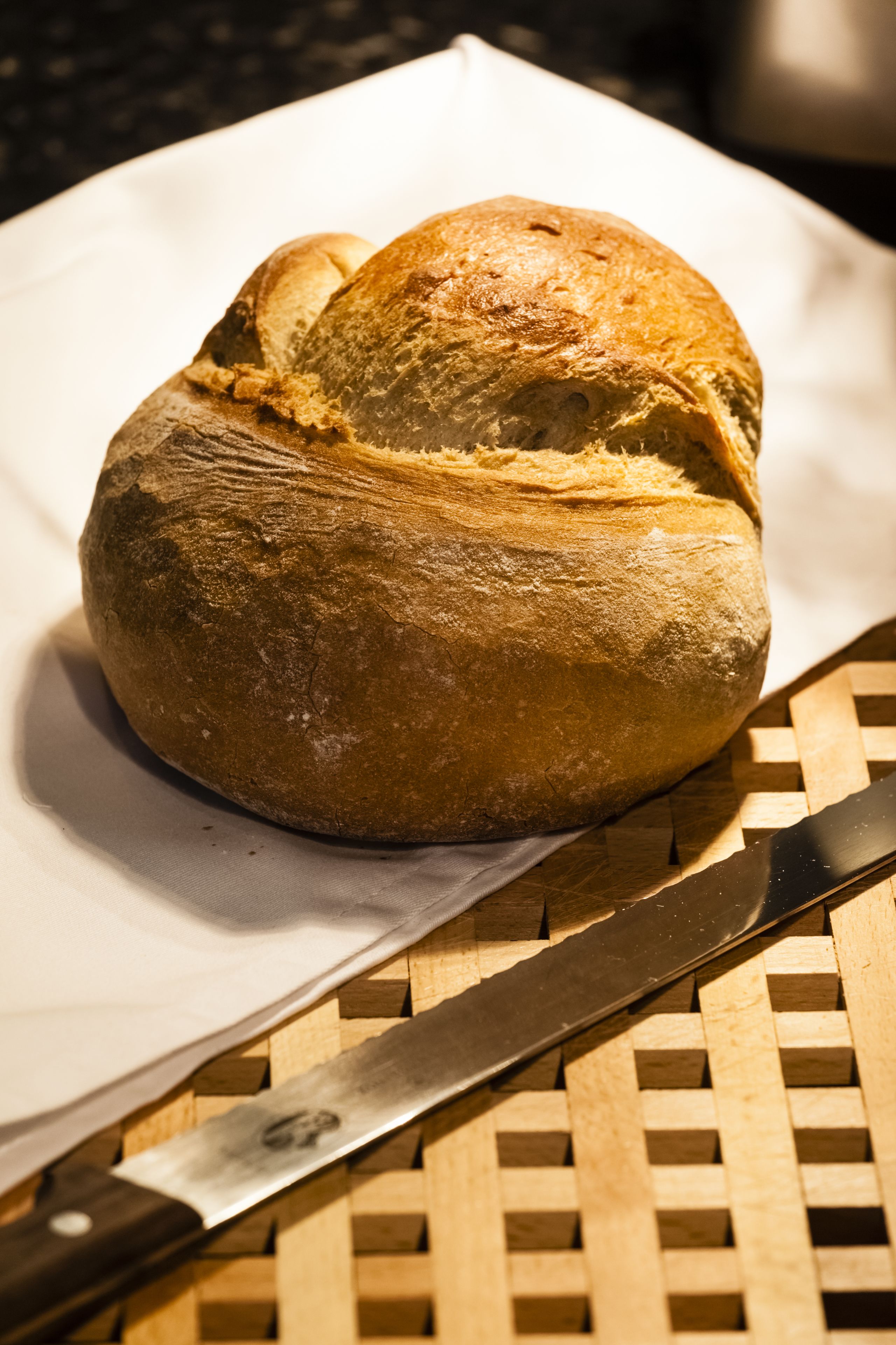 Una barra de pan sobre una tabla de cortar tejida, con un cuchillo a un lado.