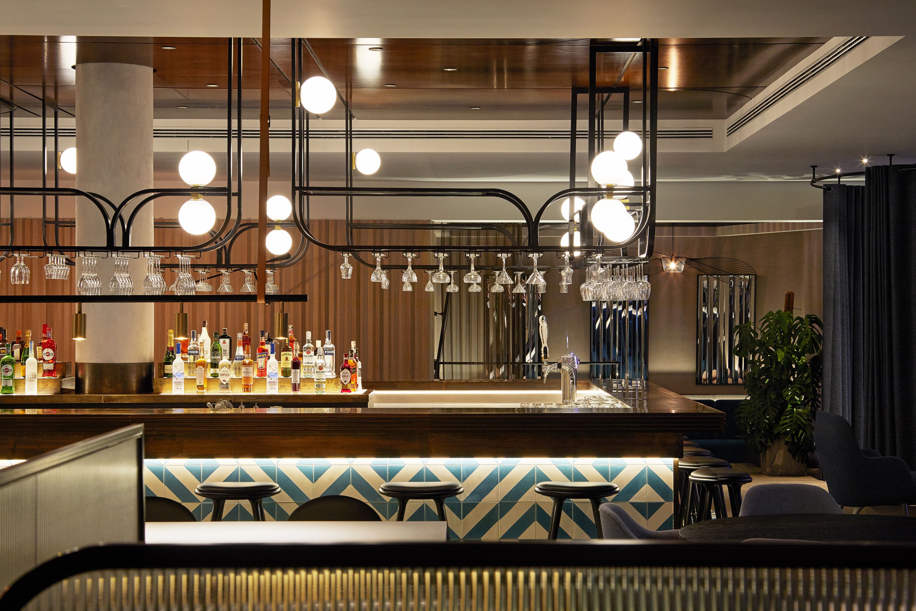 A bar area with a counter displaying various bottles and glasses, a seating area with stools, and a large potted plant.