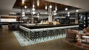 A modern bar area with a bar counter, stools, and hanging light fixtures.