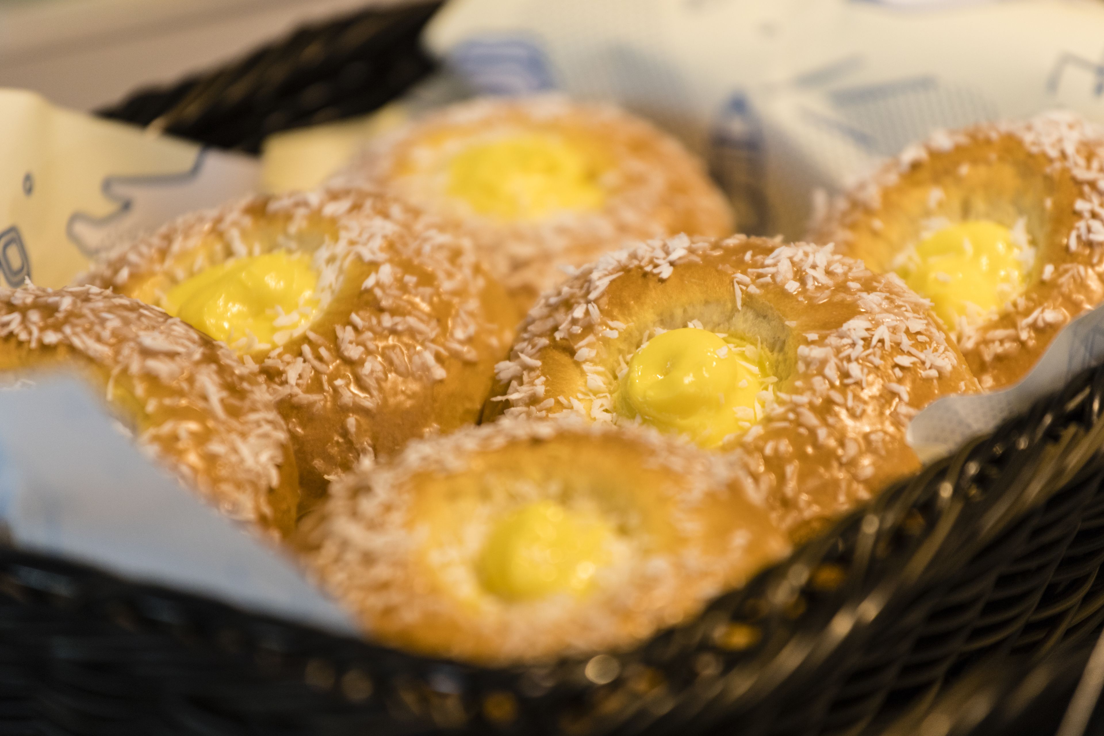 A basket of pastries with a golden-brown crust and a yellow filling, possibly butter or custard, topped with shredded coconut.