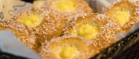 Una cesta de pasteles con corteza dorada y relleno amarillo, posiblemente de mantequilla o crema pastelera, cubierta con coco rallado.