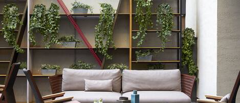 Un espace de détente extérieur moderne, aménagé avec un canapé et des fauteuils, une table basse, et un décor composé de jardins verticaux et d’étagères.
