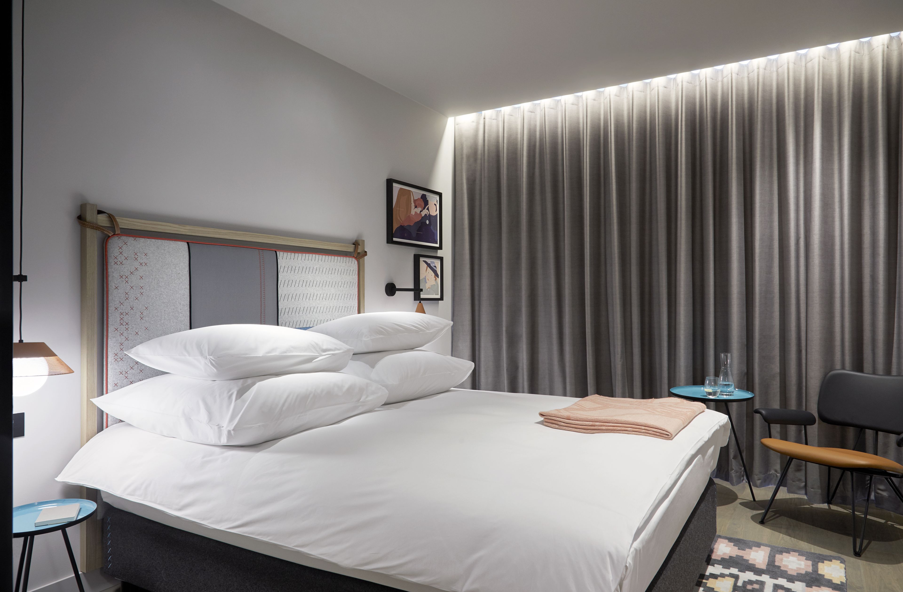 A modern hotel room with a large bed, a small table, a chair, and a large window with curtains.