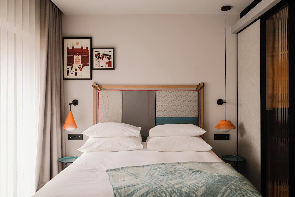 A neatly made bed with white linens, two bedside tables with orange lamps, and two framed pictures on the wall.