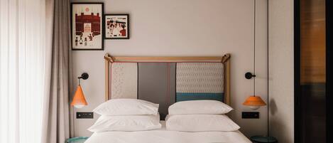 A neatly made bed with white linens, two bedside tables with orange lamps, and two framed pictures on the wall.