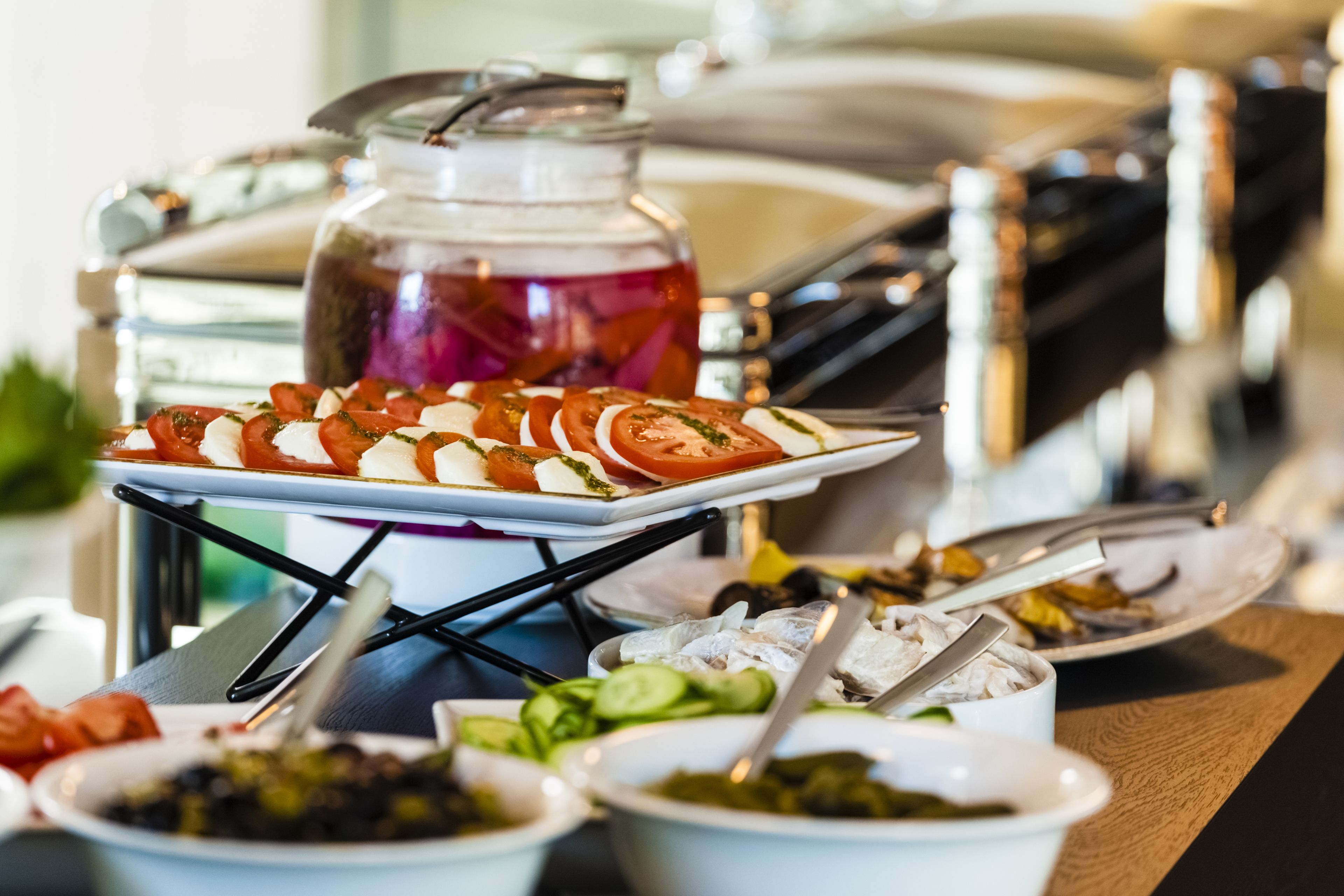 A buffet with various dishes, including sliced tomatoes, cucumbers, and a jar of pickles.