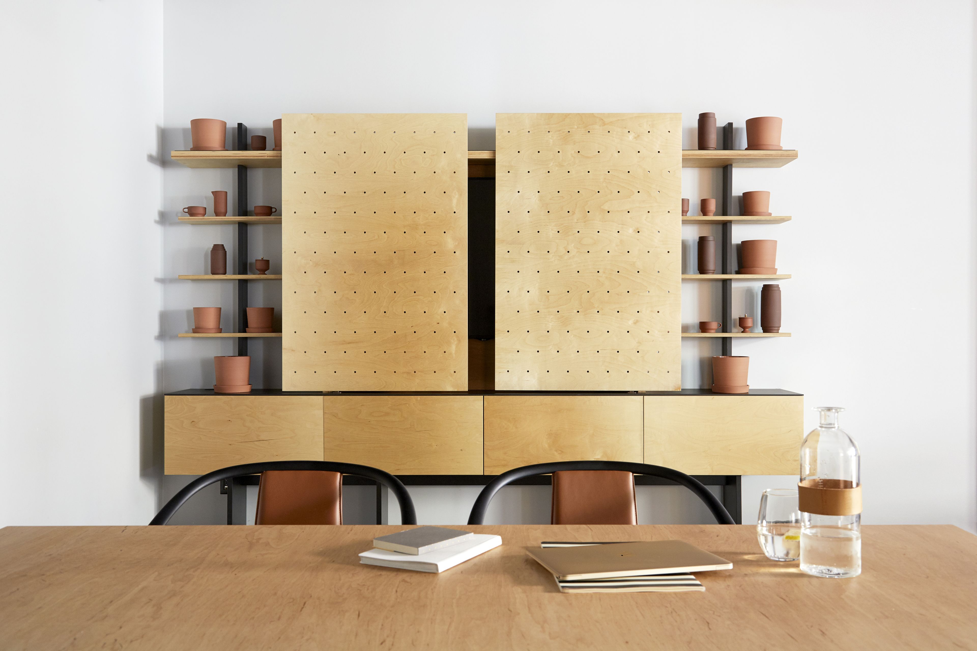 A wooden table with chairs, a bookshelf with terracotta pots, and a glass bottle on the table.