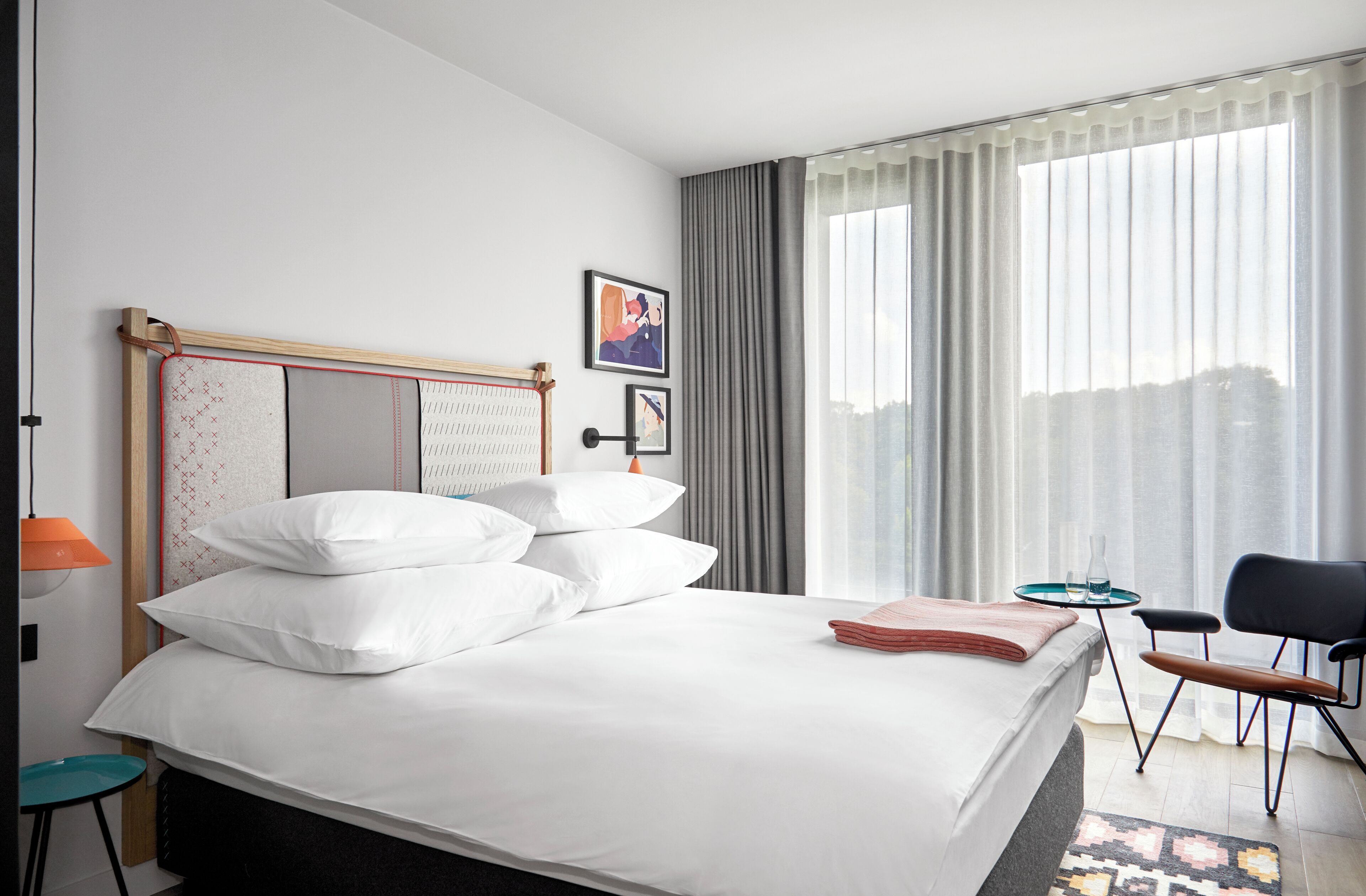 Habitación de hotel con cama, una silla, una mesita y ventana con cortinas.