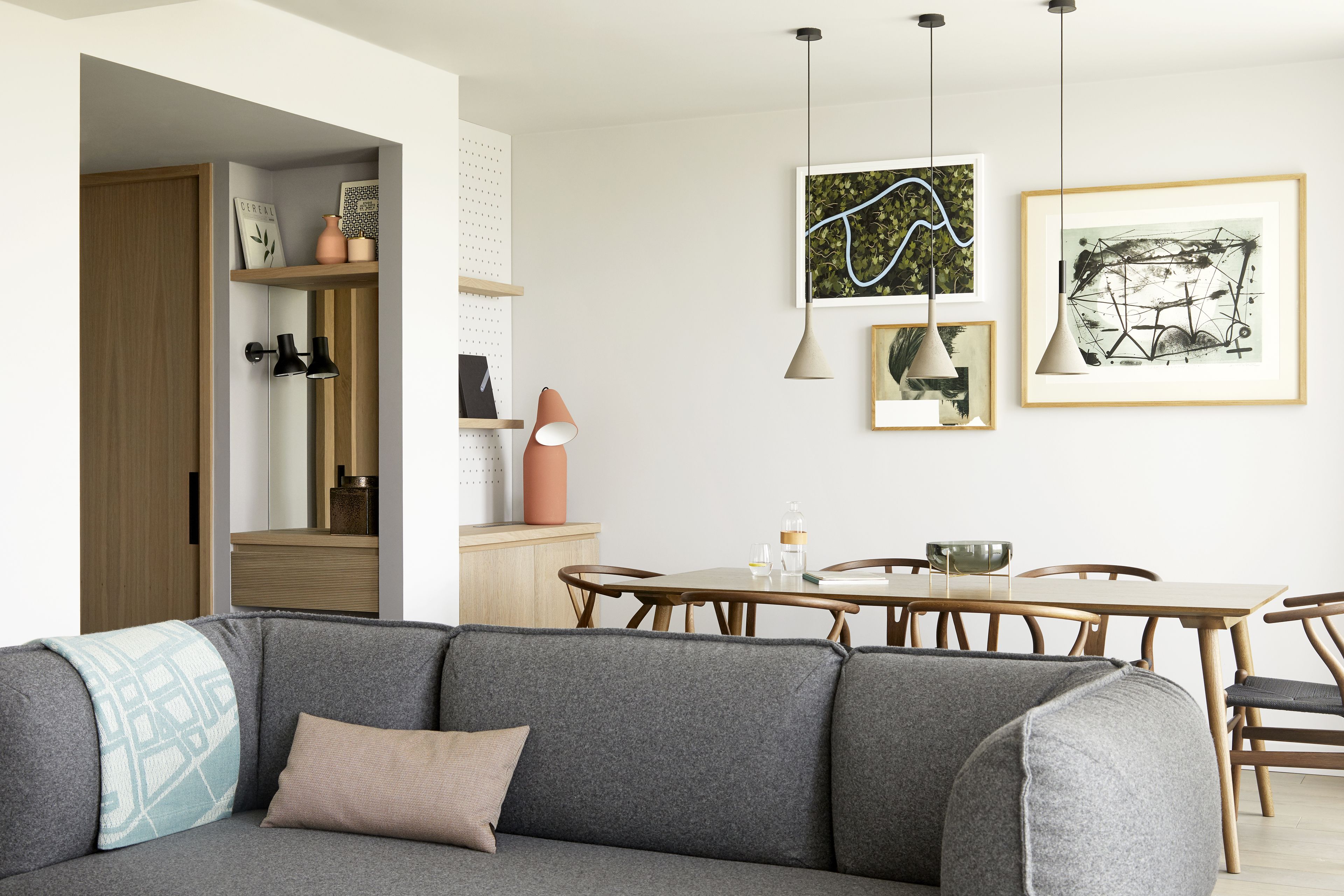 A modern living room with a grey sofa, wooden dining table, and pendant lighting.