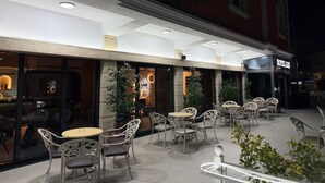 An outdoor seating area with tables and chairs, a building with a sign that reads 'HOTEL LASS,' and a storefront with a sign that reads 'LISS.' - Hotel Liss (Lezhe)